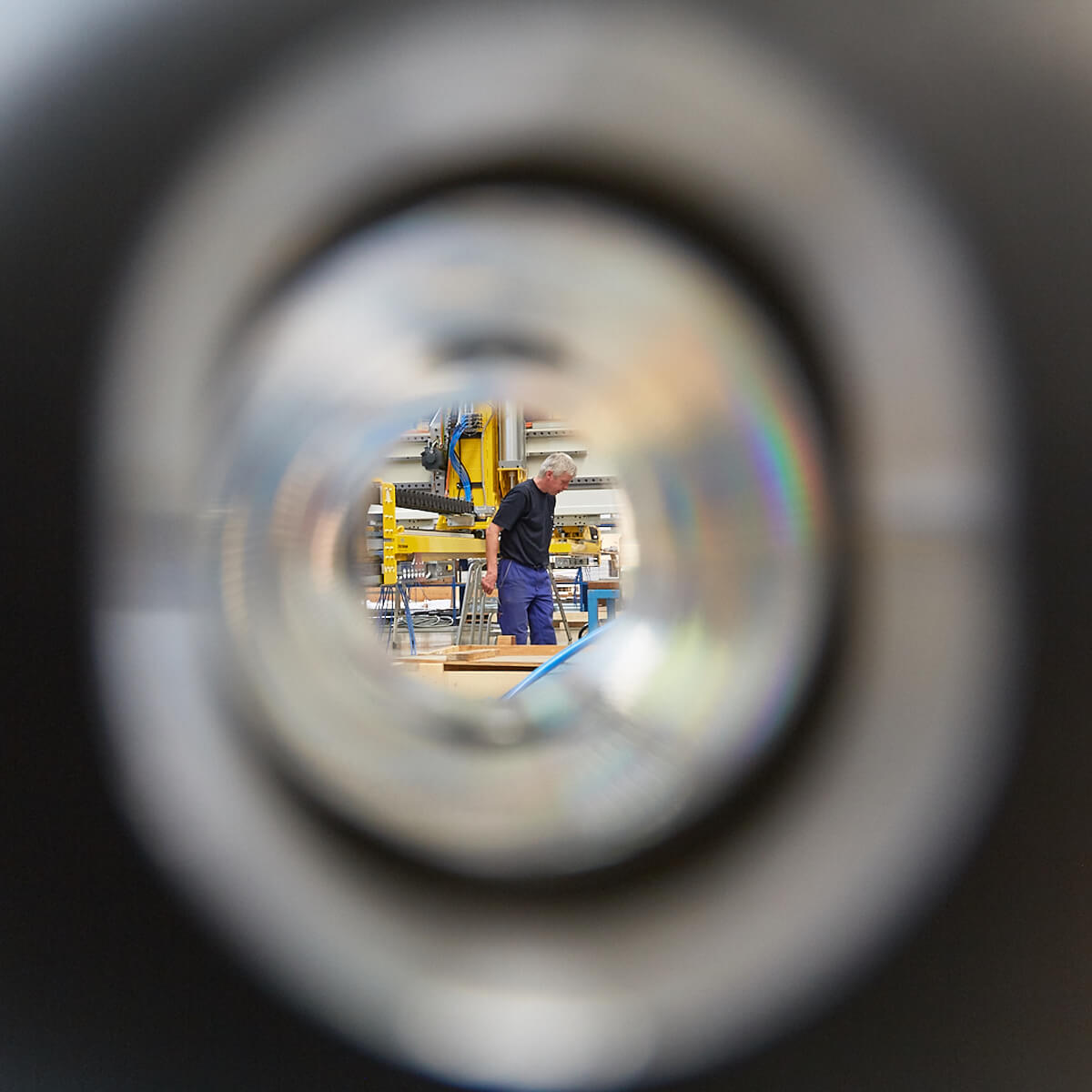 Blick durch ein Rohr auf einen Mann in einer Werkstatt, der arbeitet.